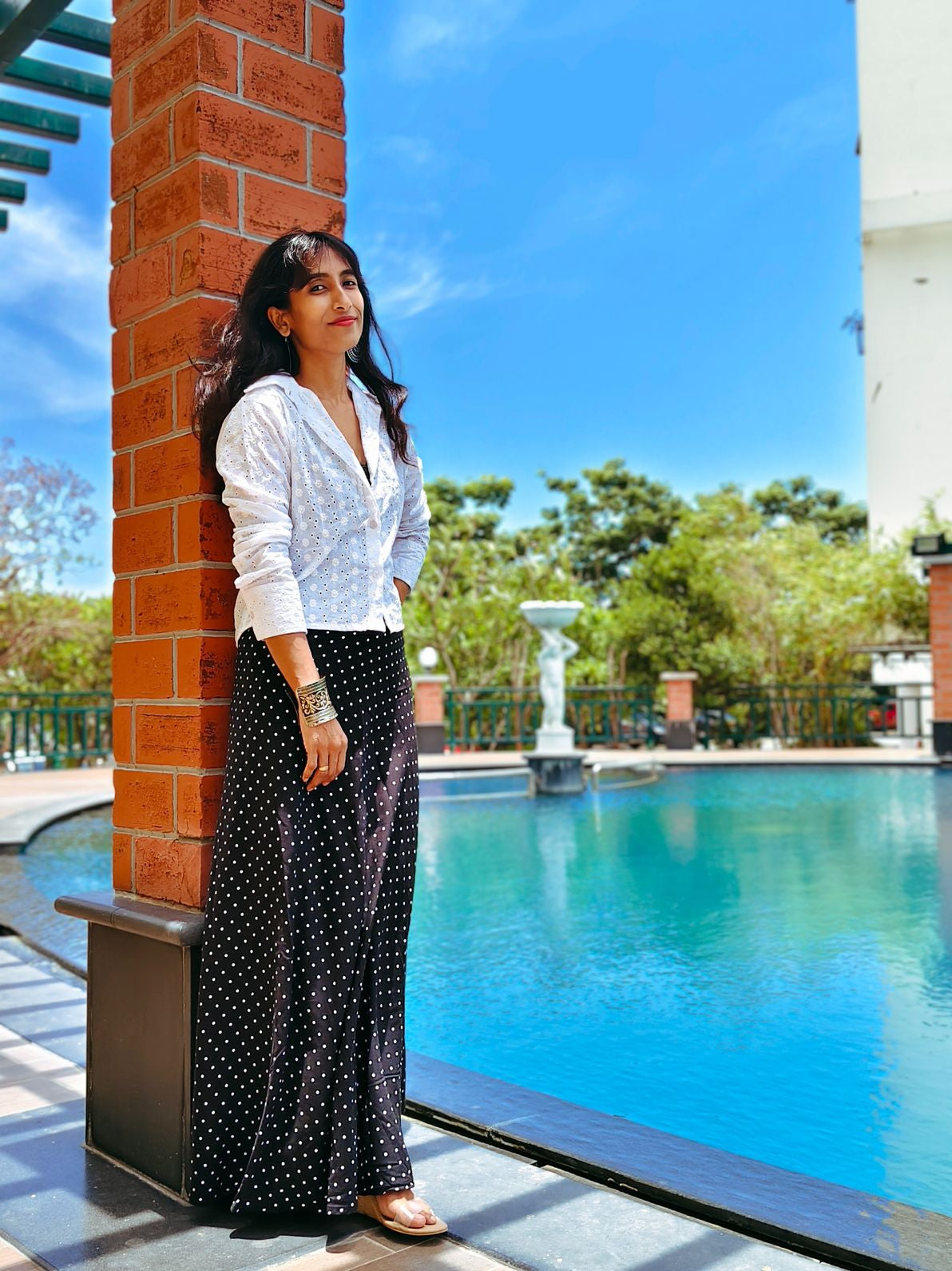 Woman standing by a pool with a fountain and trees in the background