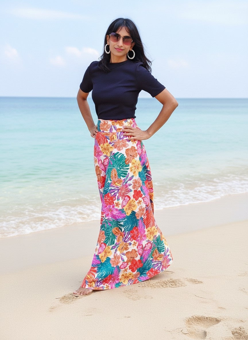 Woman in a floral skirt and black top standing on a beach with ocean in the background