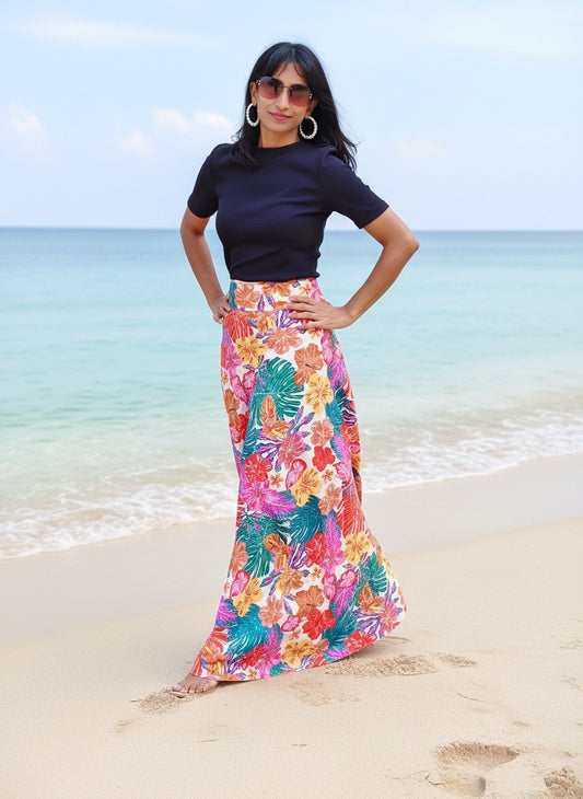 Woman in a floral skirt and black top standing on a beach with ocean in the background