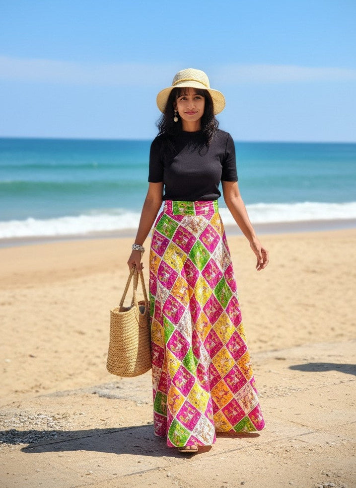 Woman in a colorful skirt and straw hat standing on a beach with ocean in the background