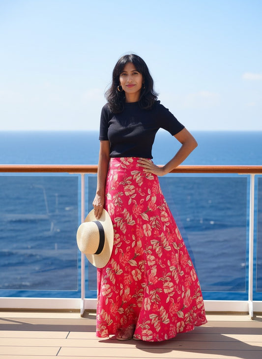 Woman in a black top and red floral skirt standing on a cruise ship deck with ocean view